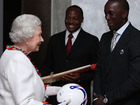 Queen happily receives autographed cricket bat from Brian Lara and autographed football from Dwight Yorke. Commonwealth Secretariat.   