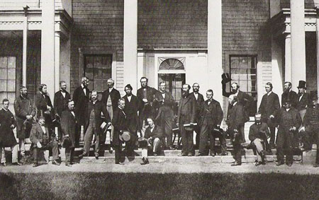 Charlottetown conference 1864 – where the present Canadian confederation began. John A. Macdonald is seated on the step, more or less in the middle. Standing at the front immediately left of Macdonald is his crucial French Canadian partner, Georges Etienne Cartier. Standing some distance to the right, at the front, is George Brown.